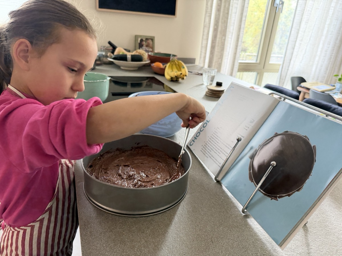 Vida strijkt het chocoladebeslag glad in de springvorm, met het kookboek ernaast